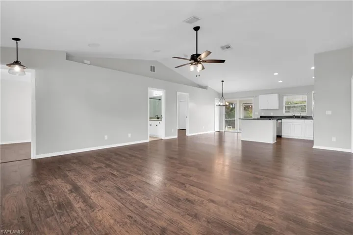 Unfurnished living room featuring hanging lights, ceiling fan, and dark wood finished floors