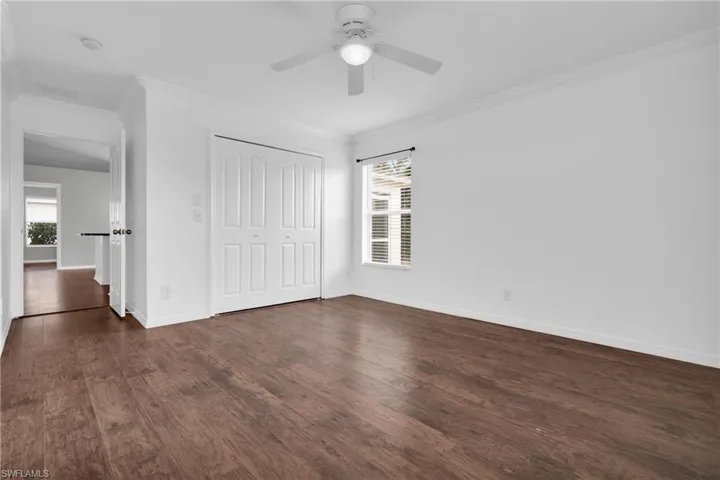 Unfurnished bedroom featuring ornamental molding, a closet, dark wood-style floors, and a ceiling fan