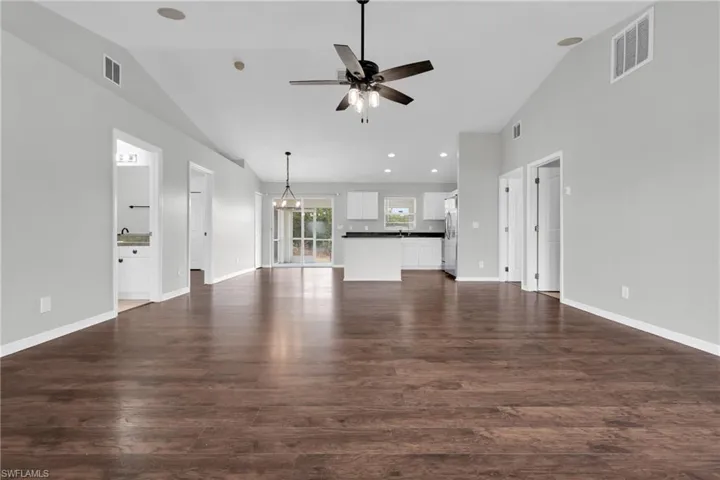 Unfurnished living room featuring vaulted ceiling, dark wood finished floors, a ceiling fan, and hanging lights