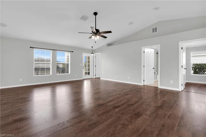 Unfurnished living room featuring a ceiling fan, dark wood-style floors, and lofted ceiling