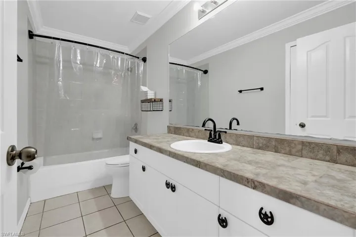 Bathroom with vanity, ornamental molding, shower / bathtub combination with curtain, and light tile patterned flooring