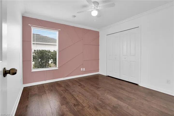 Unfurnished bedroom featuring ornamental molding, ceiling fan, dark wood-style floors, and a closet