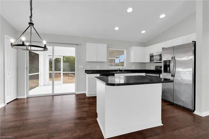 Kitchen featuring stainless steel appliances, white cabinetry, a center island, dark countertops, and lofted ceiling