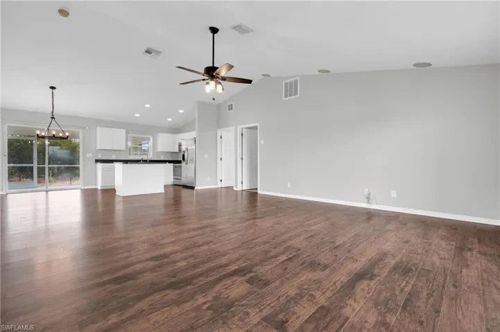 Unfurnished living room featuring hanging lights, a high ceiling, dark wood-type flooring, and ceiling fan