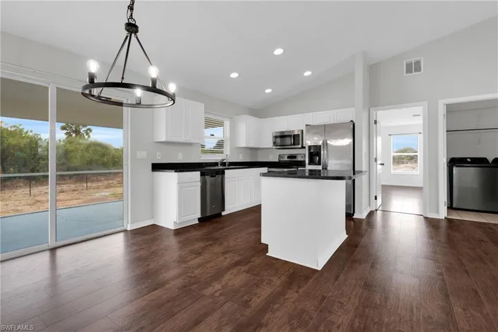 Kitchen with vaulted ceiling, white cabinets, washer / clothes dryer, a center island, and a chandelier