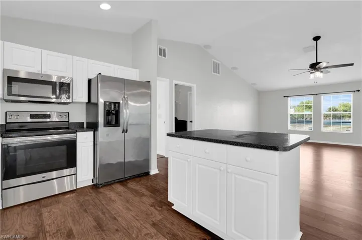 Kitchen featuring stainless steel appliances, white cabinets, dark wood-type flooring, and vaulted ceiling