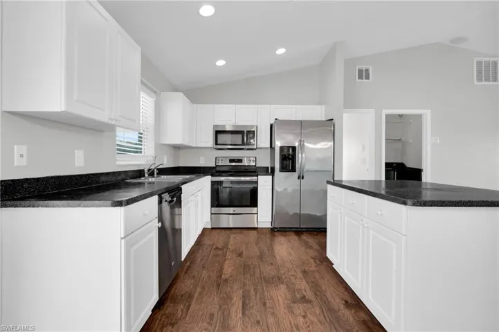 Kitchen featuring dark countertops, stainless steel appliances, white cabinetry, dark wood-style floors, and lofted ceiling