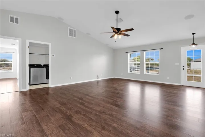 Unfurnished living room featuring dark wood-type flooring, a ceiling fan, washing machine and dryer, and vaulted ceiling