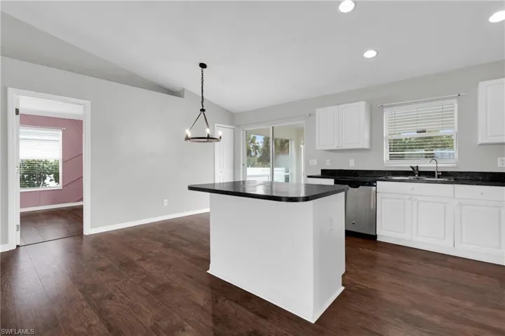 Kitchen with dark countertops, white cabinetry, a center island, lofted ceiling, and dishwasher