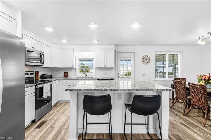 Open-concept living area featuring a kitchen island with stone countertops, recessed lighting, wood-finish flooring, and white walls