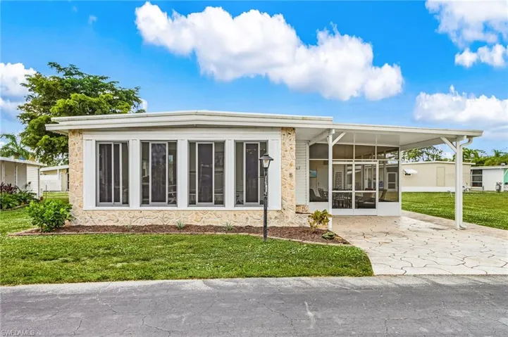 Single-story residence featuring a stone veneer facade, multiple front-facing windows, a covered and screened entryway, an attached carport, and a patterned concrete driveway
