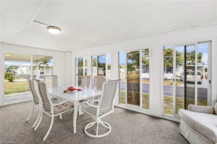 Enclosed sunroom featuring multiple sliding glass doors, textured carpet flooring, a white ceiling with recessed lighting, and a neutral color palette