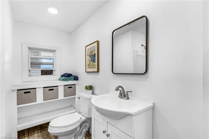 Bathroom featuring a white vanity with integrated sink, rectangular mirror, and wood-finish flooring