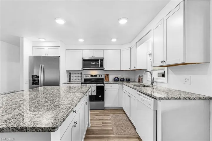 Contemporary kitchen featuring white cabinetry, stainless steel appliances, granite countertops, and wood-finish flooring