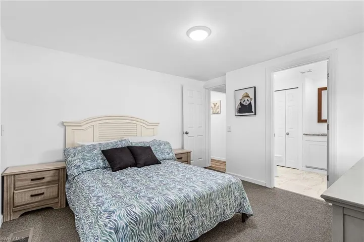 Carpeted room with white walls, featuring a light-colored headboard and two wood-finish nightstands