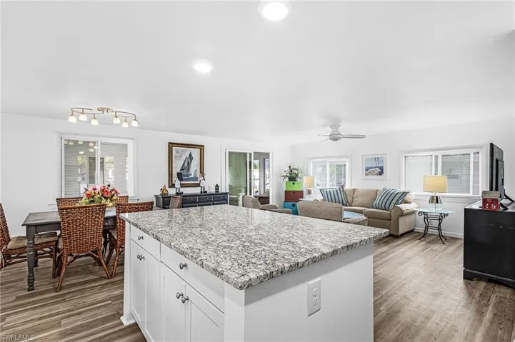 Bright kitchen featuring an island with granite countertops, wood-finish flooring, white cabinetry, stainless steel appliances, and recessed lighting