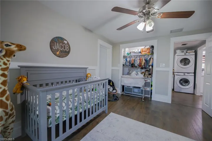 Bedroom featuring dark hardwood / wood-style flooring, stacked washing maching and dryer, ceiling fan, a crib, and a closet