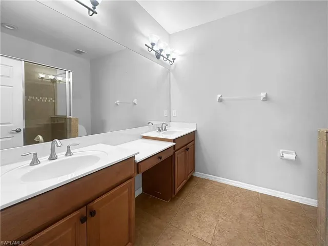 Full bathroom featuring double vanity, baseboards, a shower stall, and tile patterned flooring