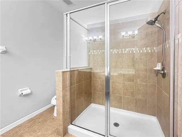 Bathroom featuring a stall shower, toilet, baseboards, and tile patterned flooring