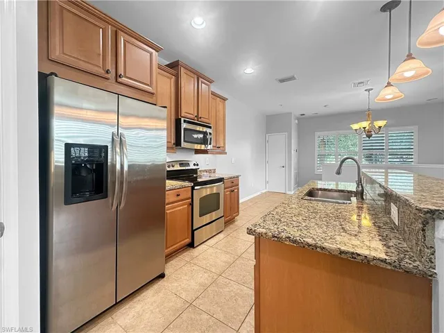 Kitchen featuring stainless steel appliances, a sink, a chandelier, brown cabinets, and recessed lighting