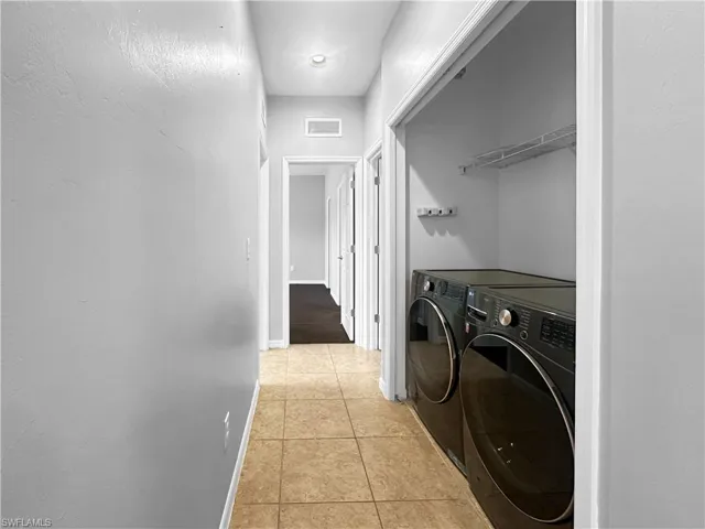 Washroom with light tile patterned floors, washing machine and clothes dryer, and baseboards