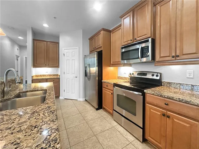 Kitchen featuring stainless steel appliances, a sink, stone countertops, light tile patterned flooring, and brown cabinets