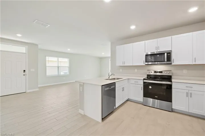 Kitchen with kitchen peninsula, light hardwood / wood-style flooring, stainless steel appliances, and white cabinets