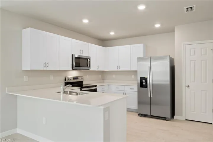 Kitchen featuring white cabinetry, kitchen peninsula, stainless steel appliances, light hardwood / wood-style floors, and sink