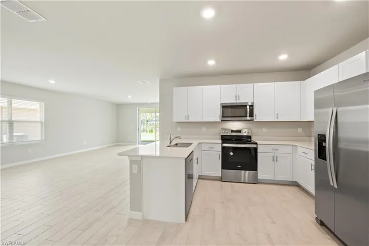 Kitchen with appliances with stainless steel finishes, light hardwood / wood-style flooring, white cabinets, sink, and kitchen peninsula