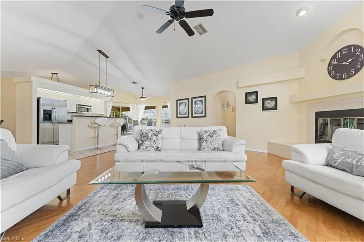 Open-concept living area featuring vaulted ceilings, wood-finish flooring, a fireplace with a tiled surround, and a kitchen with a breakfast bar