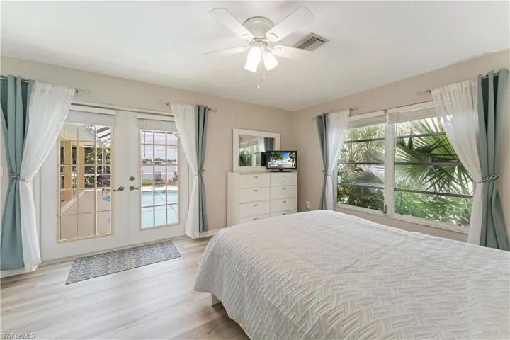 Spacious room featuring wood-finish flooring, a ceiling fan, and French doors opening to an outdoor pool area
