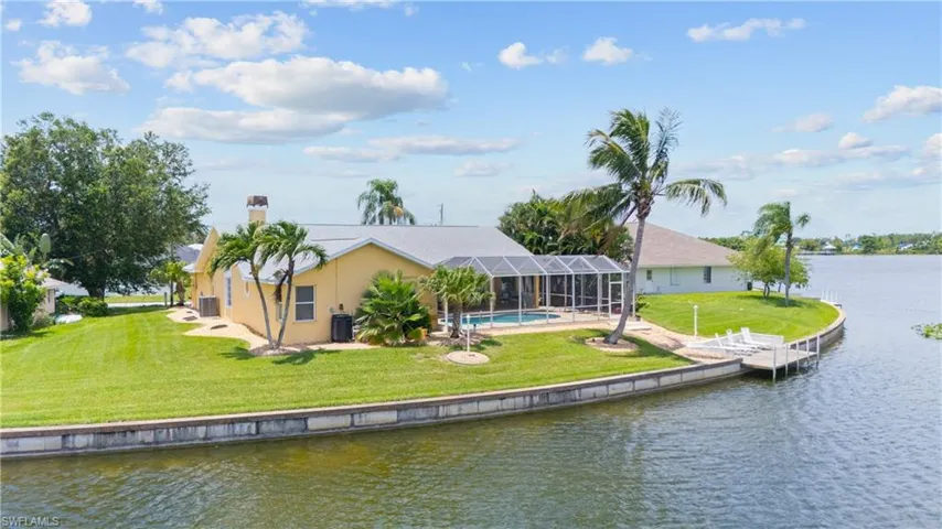 Waterfront home featuring a screened-in pool enclosure, private dock with seating, and mature palm trees