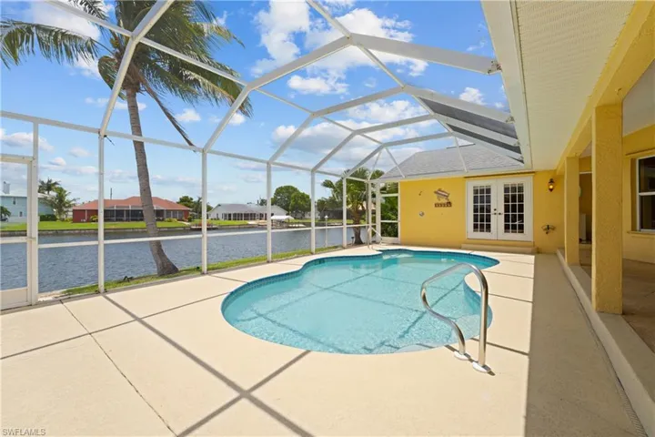 Screened pool area featuring a freeform pool with a handrail, a concrete patio, and direct access to a canal