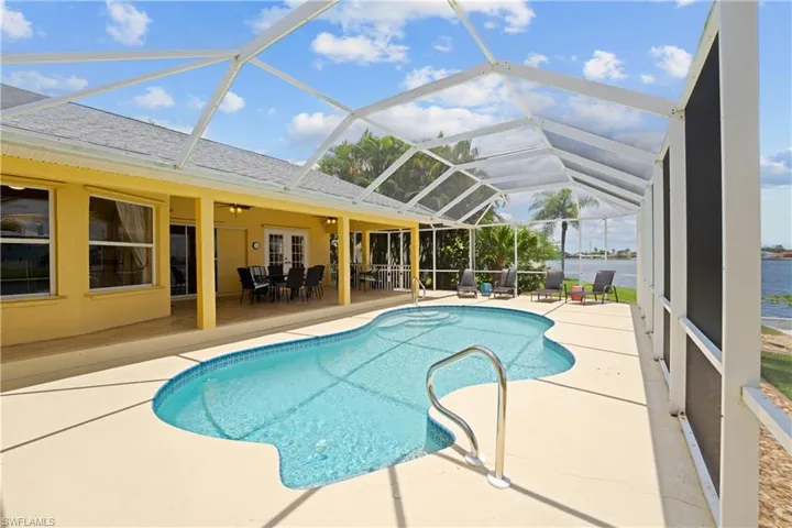 Screened lanai featuring a freeform swimming pool with steps, a concrete pool deck, and direct water frontage