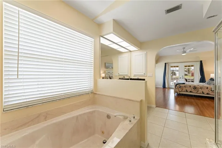 Jetted soaking tub with a tiled surround, complemented by a large window with horizontal blinds