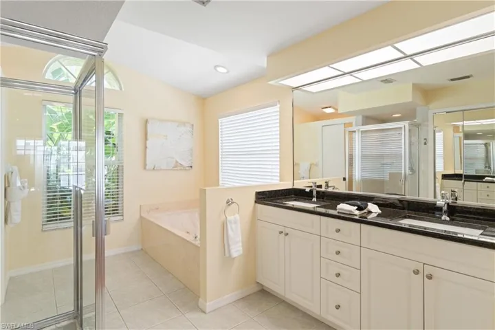 Bathroom featuring a double vanity with dark countertops, a large mirror, a separate glass-enclosed shower, a built-in tub, and tiled flooring