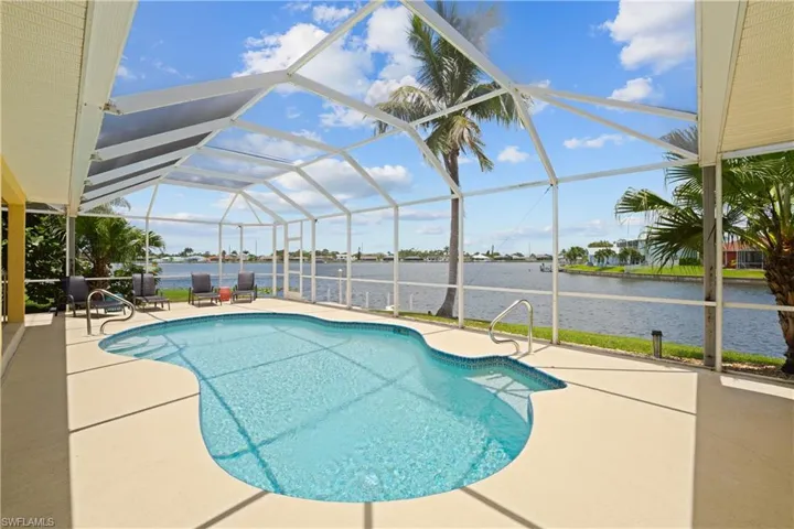 Screened-in outdoor pool area featuring a freeform pool with integrated steps, a spacious concrete paver deck, and direct waterfront access