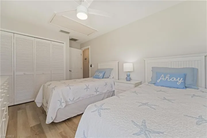 Bedroom featuring light wood-finish flooring, white louvered closet doors, a white ceiling fan with integrated lighting, and a neutral wall color