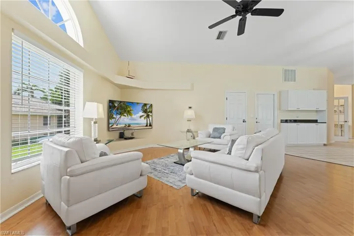 Living area featuring vaulted ceilings, wood-finish flooring, a prominent arched window, and a ceiling fan
