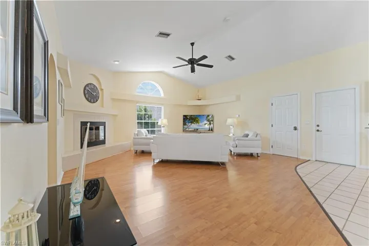 Spacious living area featuring wood-finish flooring, a fireplace with a decorative mantel, vaulted ceilings, and an arched transom window