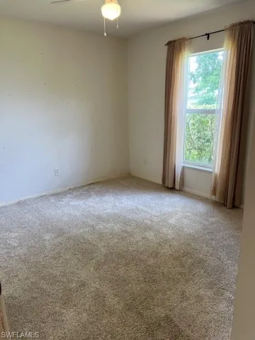 Carpeted spare room featuring ceiling fan and a healthy amount of sunlight