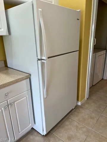 Kitchen with white cabinetry, light tile patterned floors, washing machine and clothes dryer, and white refrigerator