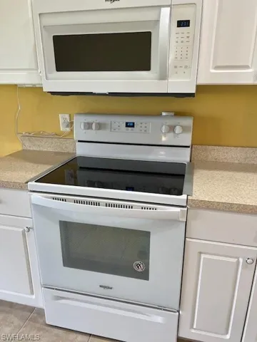 Kitchen featuring white cabinetry, light tile patterned floors, and white appliances