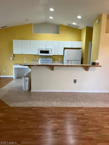 Kitchen with a kitchen breakfast bar, refrigerator, vaulted ceiling, white cabinetry, and light tile patterned floors