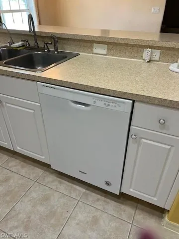 Kitchen with backsplash, sink, light tile patterned floors, white dishwasher, and white cabinetry