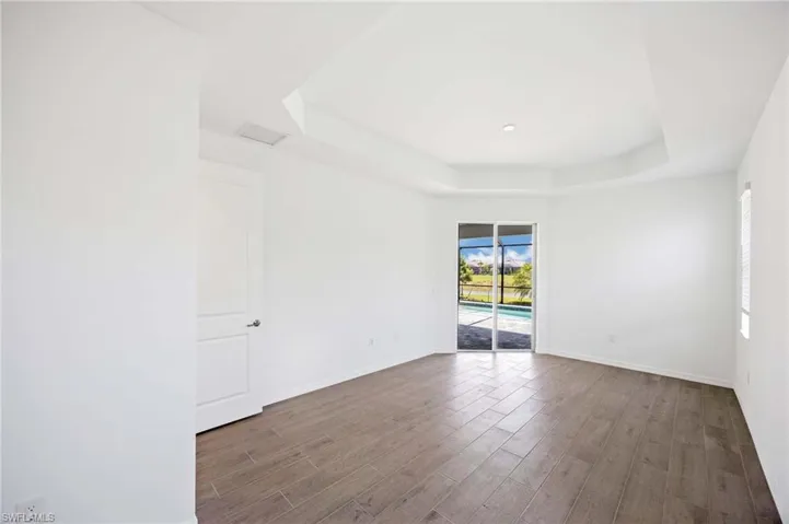 Empty room featuring baseboards, a raised ceiling, wood finished floors, and visible vents