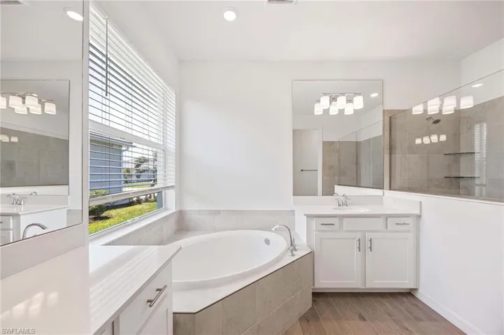 Bathroom featuring a bath, walk in shower, wood finished floors, two vanities, and a sink