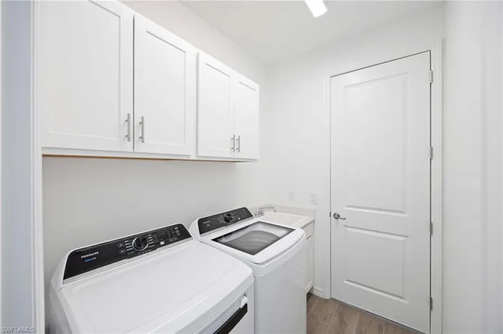 Clothes washing area featuring a sink, washing machine and dryer, cabinet space, and dark wood-type flooring