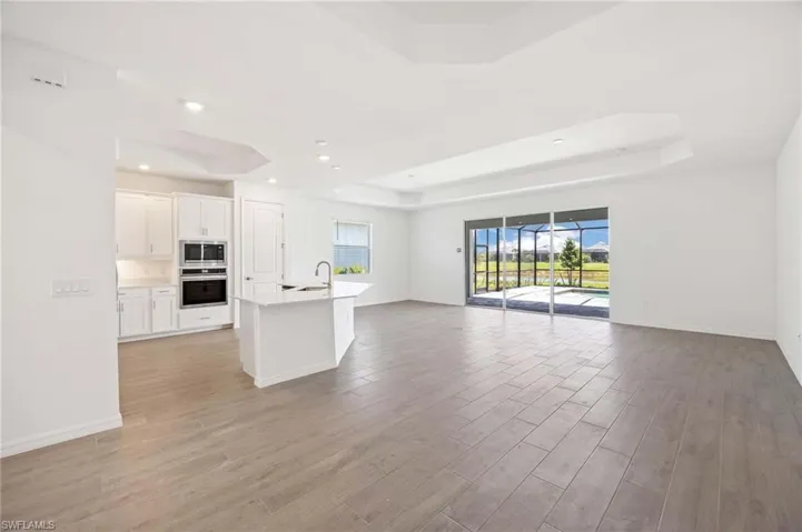 Unfurnished living room with baseboards, a sink, a raised ceiling, and light wood finished floors