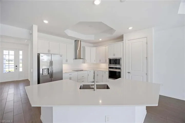 Kitchen featuring a spacious island, wall chimney exhaust hood, white cabinets, a sink, and stainless steel appliances